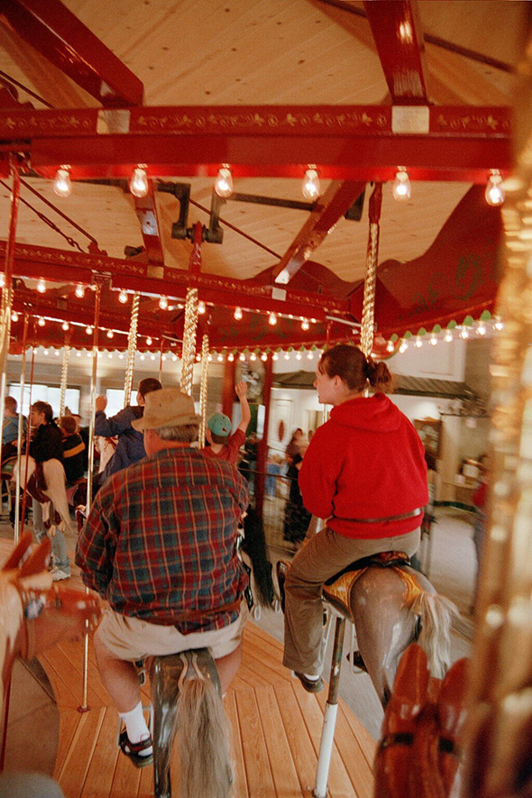 Man and girl ride carousel horses.